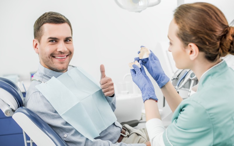 selective focus happy man showing thumb female dentist holding teeth